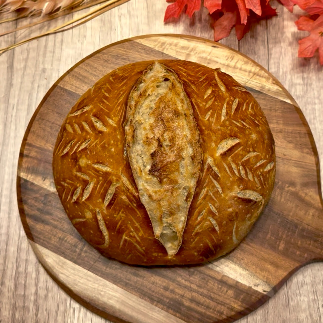 Loaf of bread on a wooden board with wheat and red leaves on a wooden surface